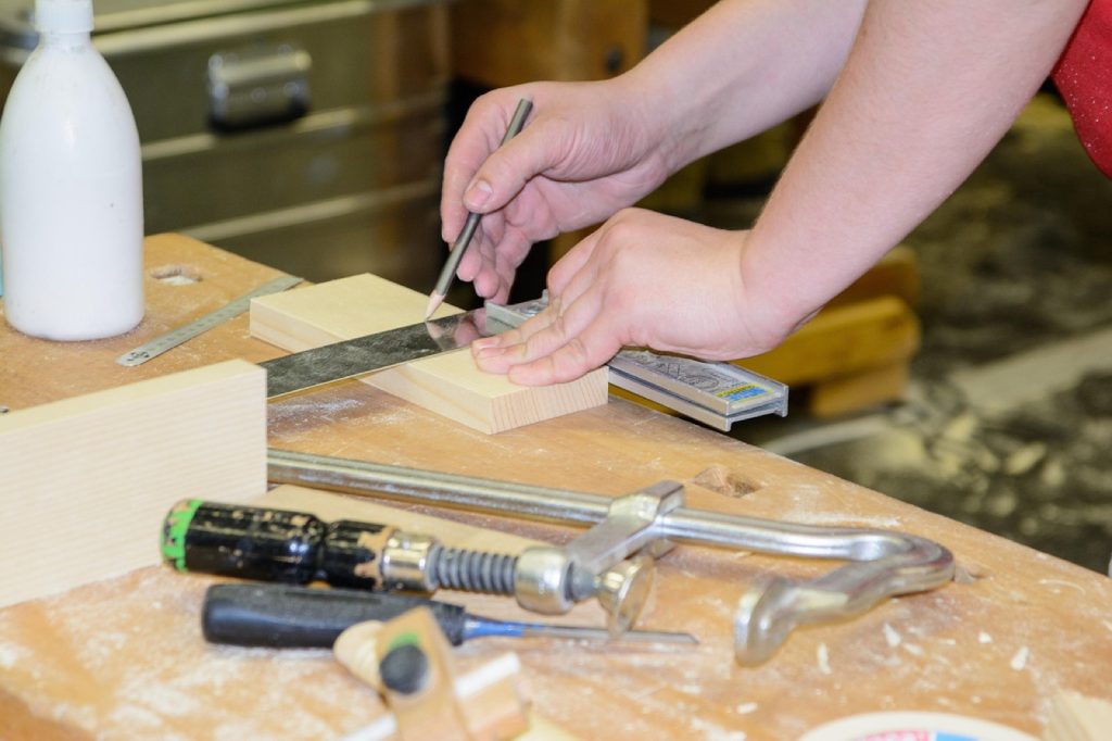 Hands marking a measurement on wood at a workshop bench